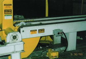 Worker operating a machine with yellow components, feeding material into it in a dimly lit factory.