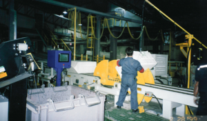 A worker operates machinery in an industrial facility with safety equipment and monitors.