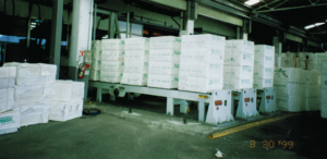 Stacks of white paper bundles on an industrial conveyor in a warehouse.