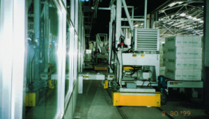 Industrial machinery on tracks next to stacked paper bundles in a warehouse.