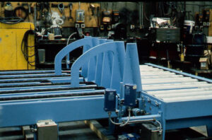 Blue conveyor system with rollers and machinery in a workshop.