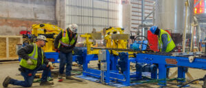 Workers installing and adjusting blue and yellow machinery in a factory setting.