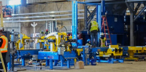 Workers in a factory assembling large blue and yellow industrial machinery.