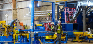 Workers in safety gear operating and assembling industrial machinery in a factory setting.