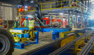 Workers assembling blue and yellow industrial machinery inside a large factory.