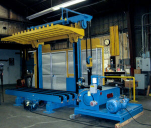 Blue and yellow industrial machine in a workshop, likely used for lifting or material handling.